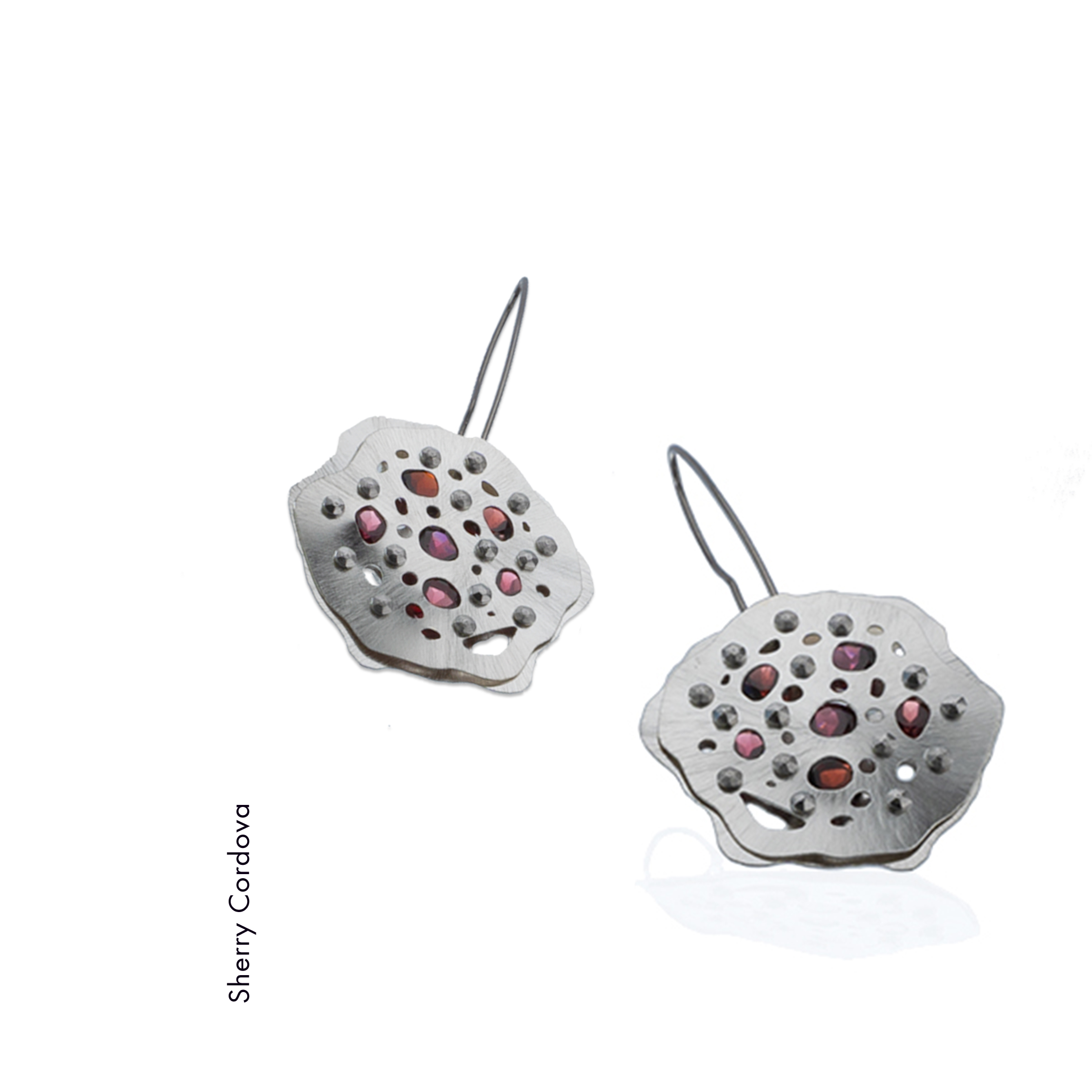 Sherry Cordova made these argentium sterling silver earrings which each contain 6 faceted garnets tension set between the two layers shaped like radiolaria. non allergenic niobium earwires finish the design