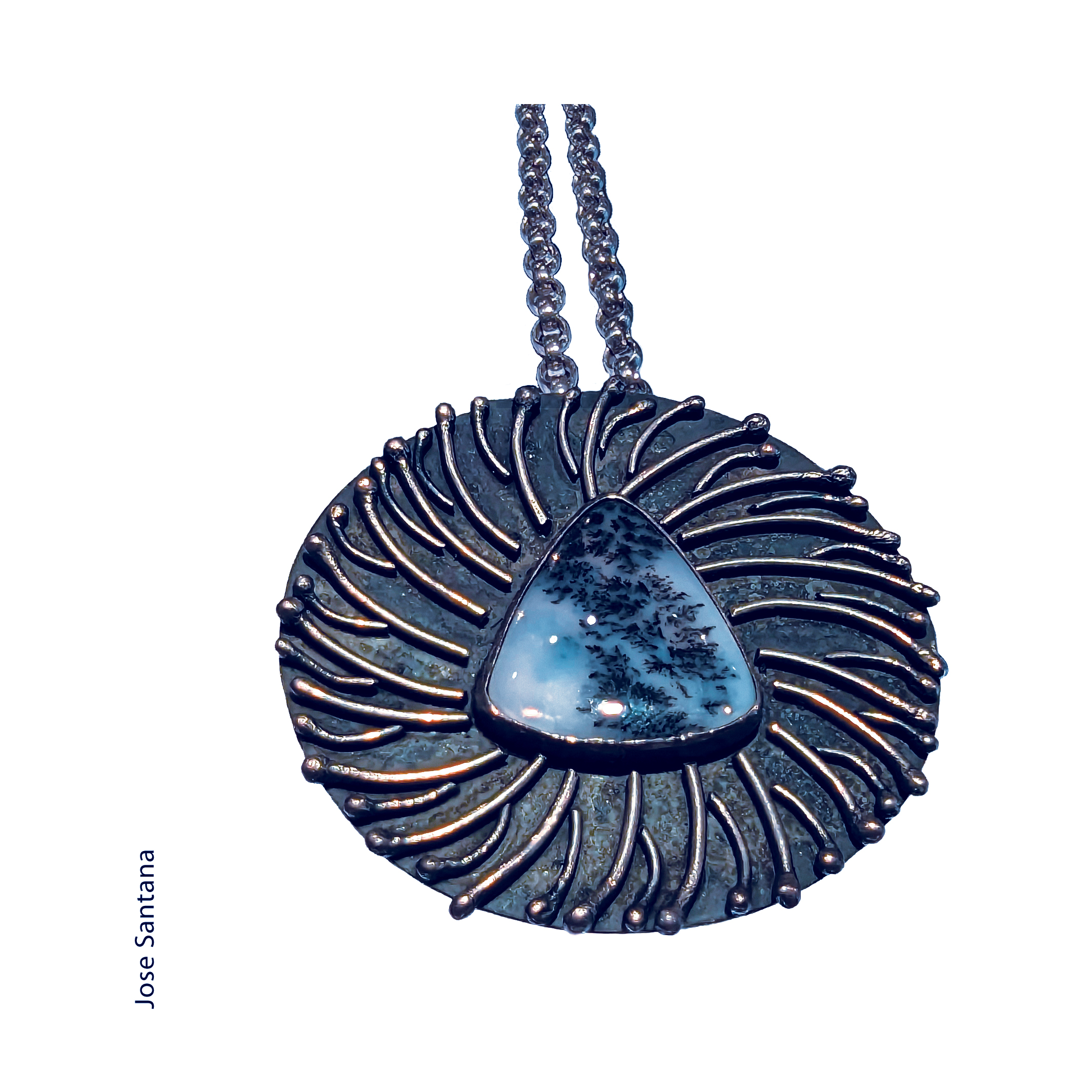angled view of a sterling silver and agate necklace by Jose Santana. The agaate is blue and white with black fern like inclusions and the pendant has ridges of silver wire that are branch like and end in balled up silver