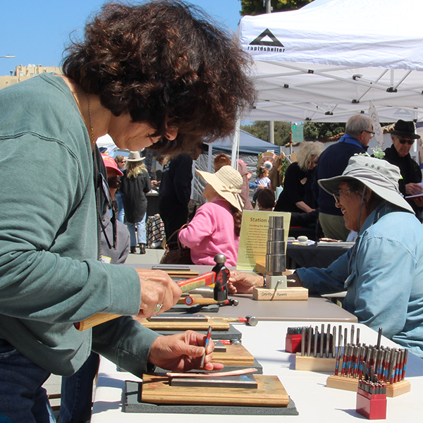 stamping a shape into a copper strip to create a bracelet at the Make A Bracelet event as part of the Monterey Museum of Art Block Party 2023