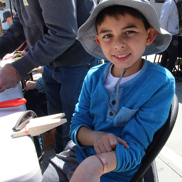 A happy young participant showing off the newly created one-of-a-kind handmade (!) bracelet at the Make A Bracelet event as part of the Monterey Museum of Art Block Party 2023