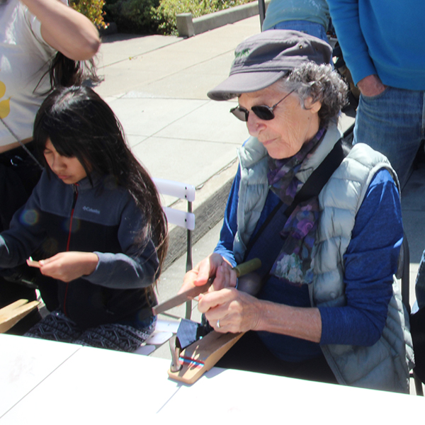 People of all ages confidently filing the ends of copper pieces to create a bracelet at the Make A Bracelet event as part of the Monterey Museum of Art Block Party 2023